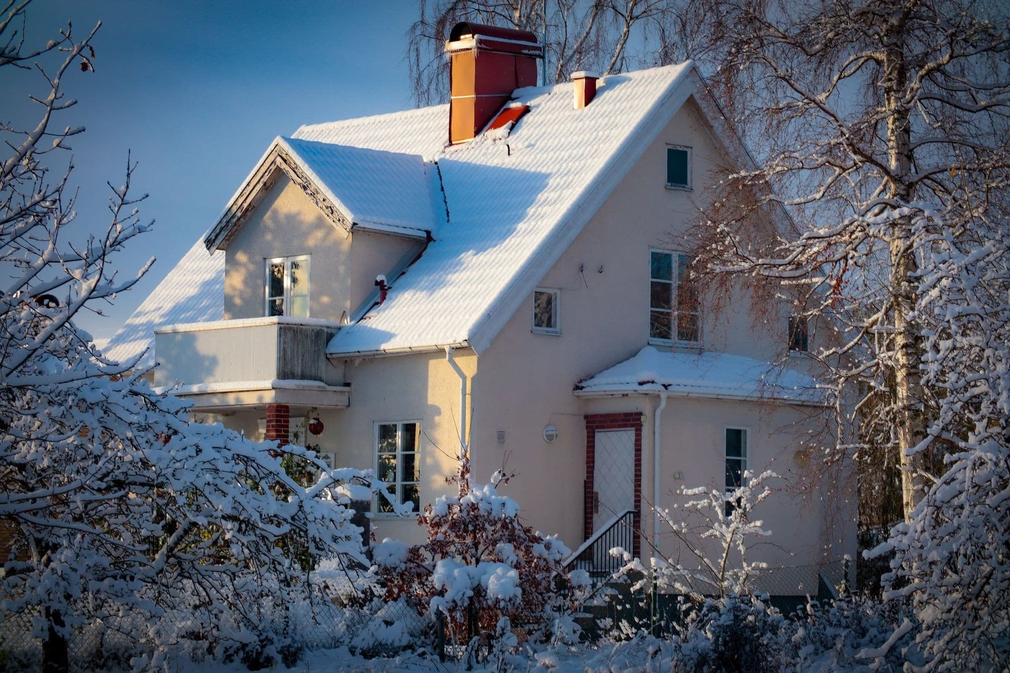 Snow-covered house with a tall brick chimney on a clear winter day