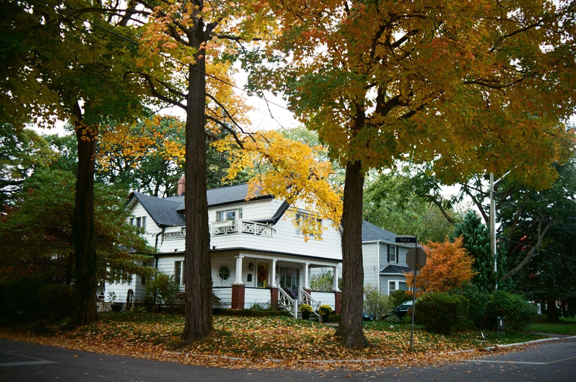 White two-story frame house with a front porch under yellow autumn maples