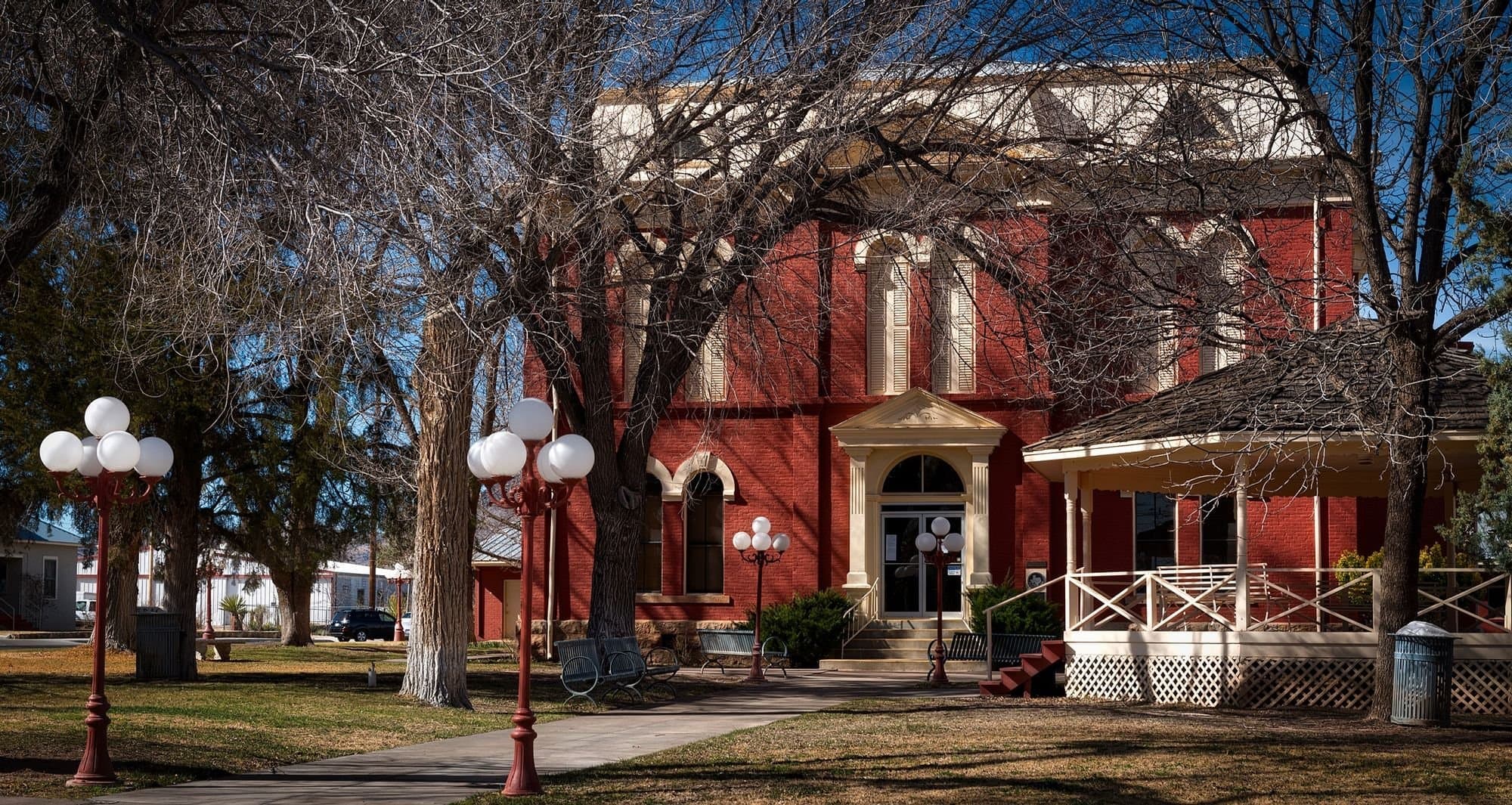 Red brick 19th-century building with a porch among tall bare trees