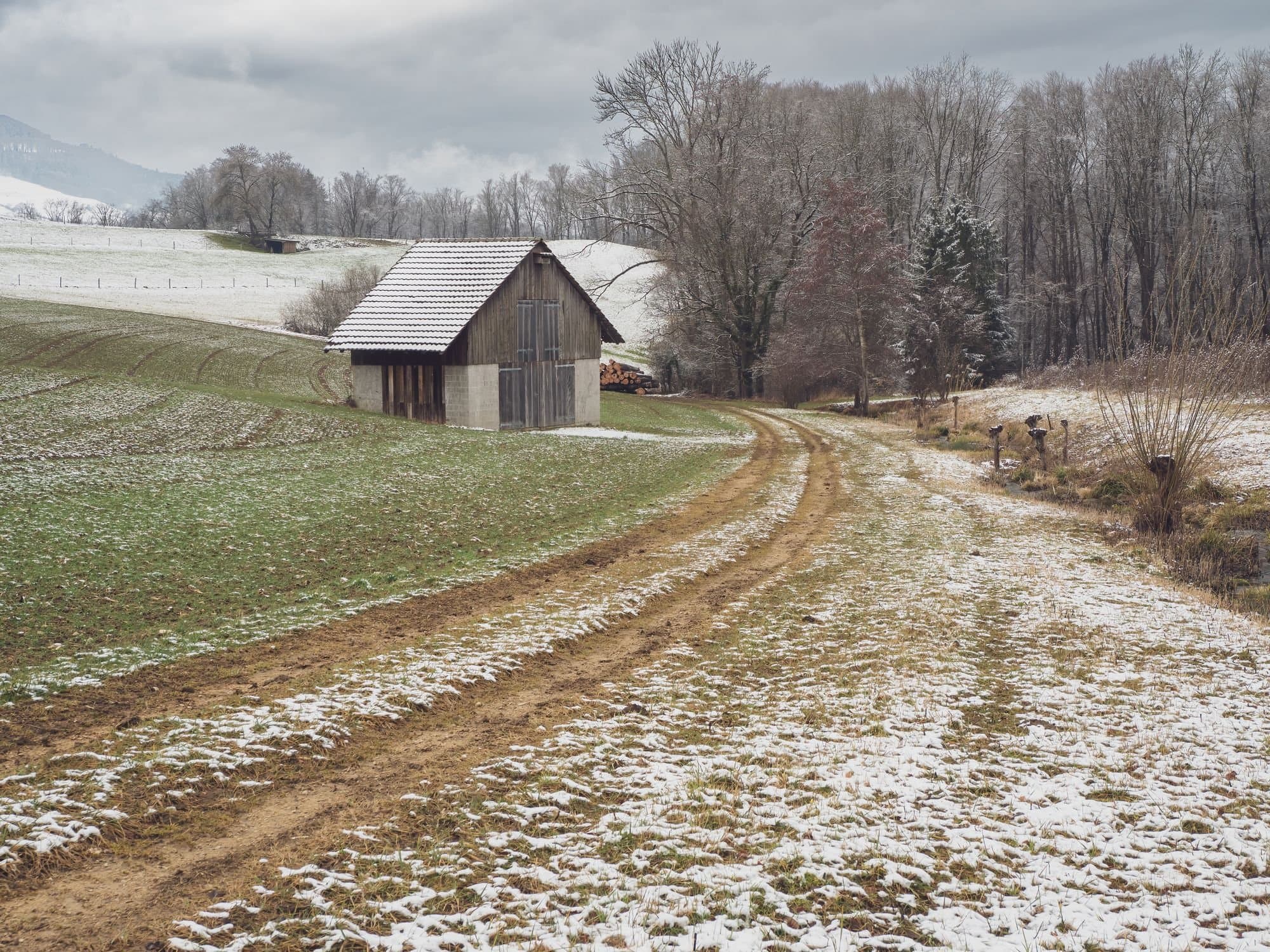 Wooden barn beside a farm lane on a snow-dusted hillside